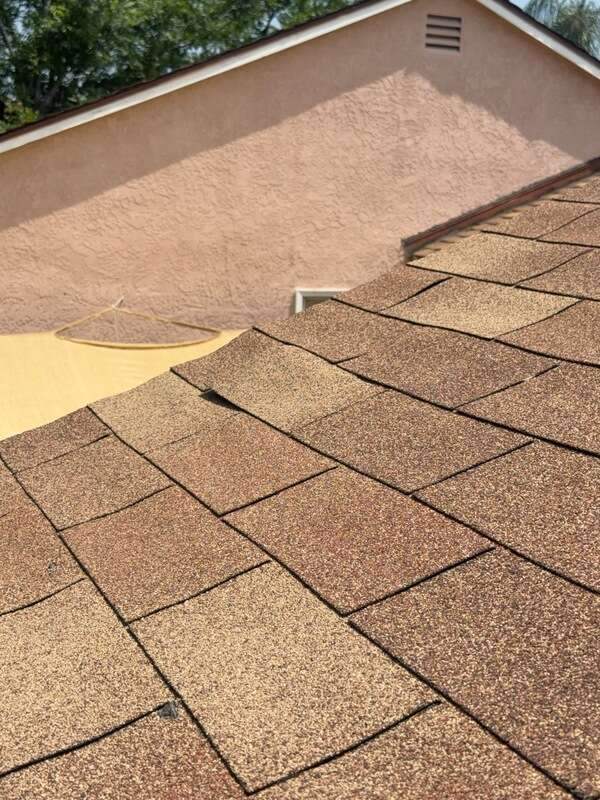 Sunlit tan-brown asphalt shingles beside a peach stucco gable wall with a small vent.