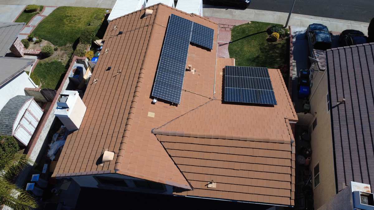 Overhead view of brown tile slopes with two dark solar panel arrays and roof vents