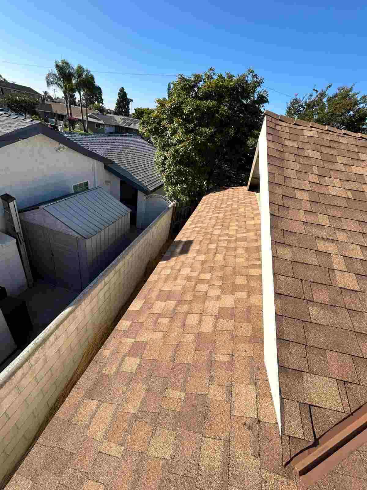 Brown shingle slopes beside a taller roof section, meeting at a white vertical junction near a block wall