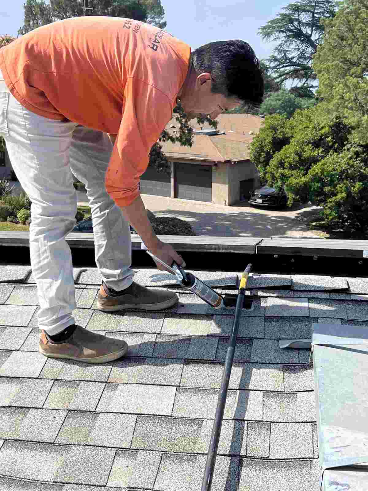Worker using a sealant applicator near the edge of a shingle roof