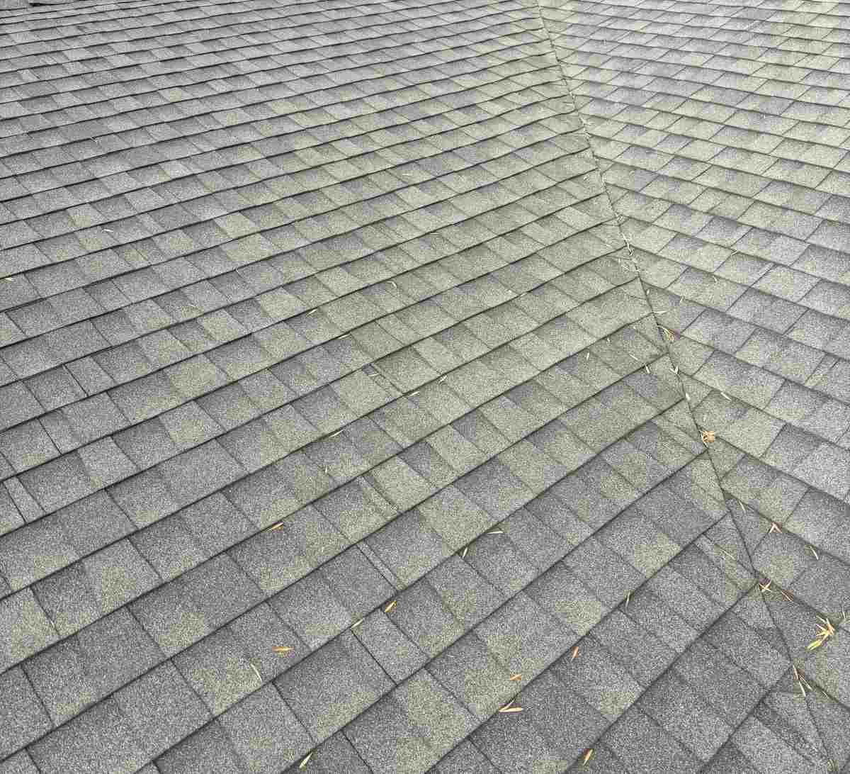 Weathered gray shingles meeting at a roof valley with a few leaves