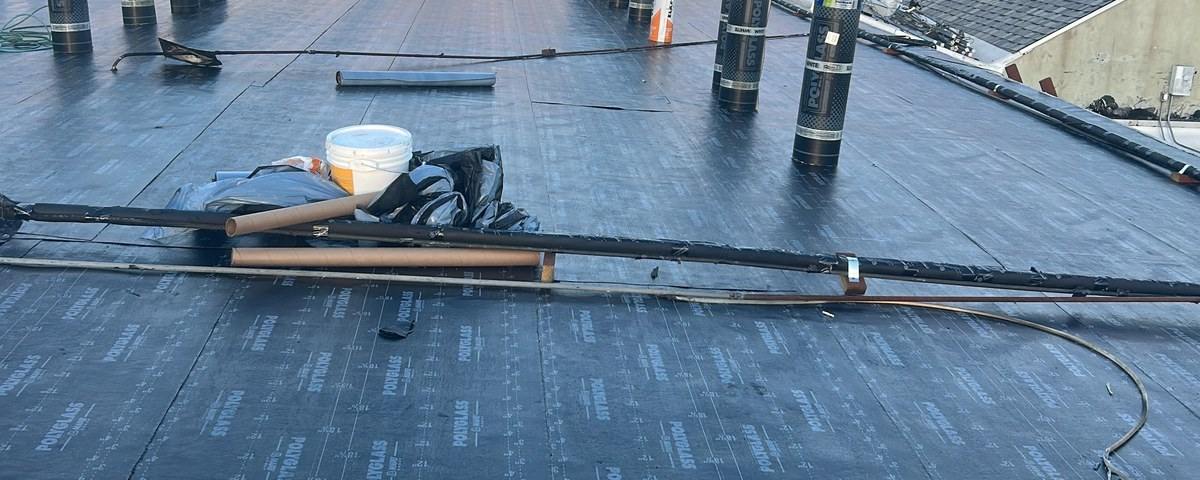 Black low-slope roof surface with material rolls, hand tools and a torch handle