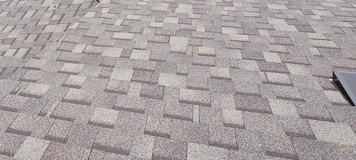 Close view of a gray-taupe shingle field with a partial low-profile roof vent